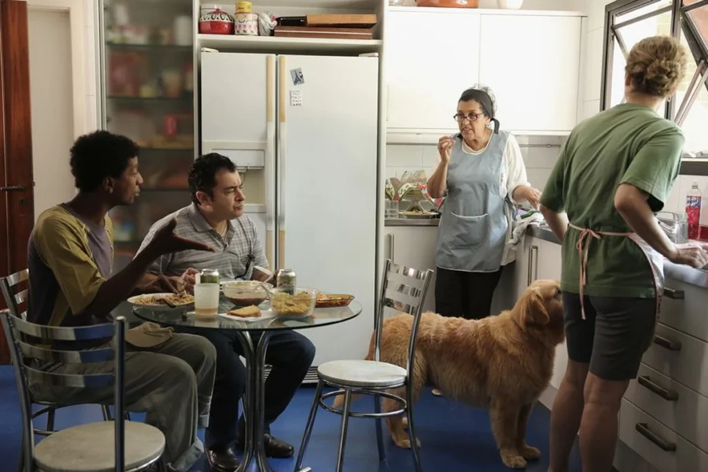 Ela dorme no quartinho, come na cozinha, cuida do filho dos outros e ouve que “é da família”. A chegada da filha escancara o que o afeto tentava esconder: existe patrão, existe hierarquia. A relação pode ser antiga, mas nunca foi igual. Foto: reprodução do filme “Que Horas Ela Volta?”